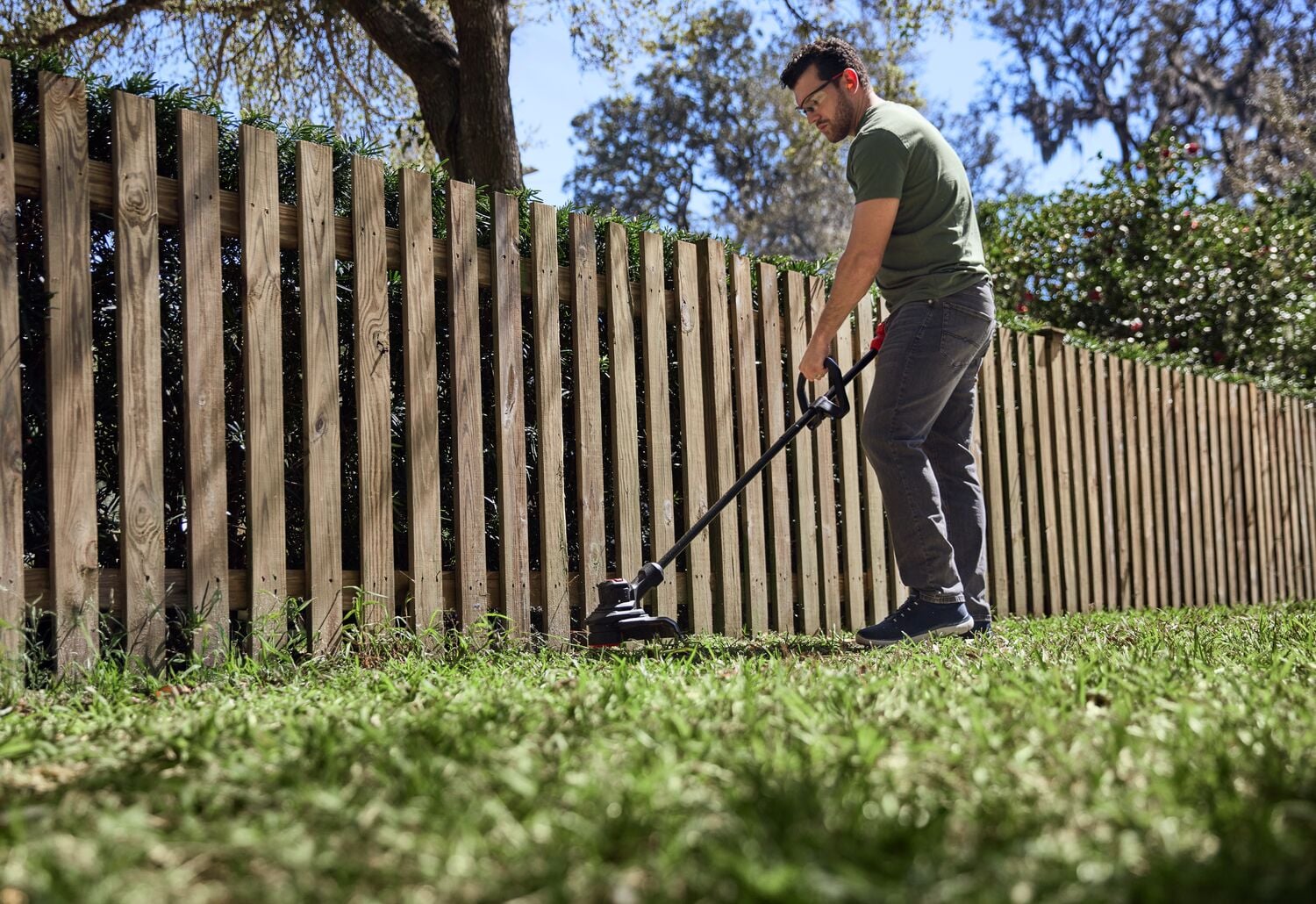 Photo of Craftsman string trimmer CMCST930P1 in use trimming grass along a wooden fence outdoors.