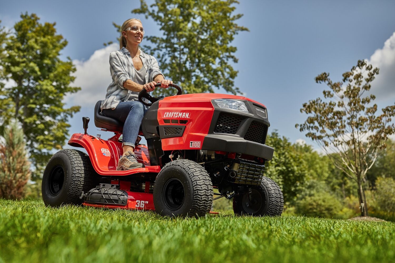 Photo of Craftsman riding lawn mower CMXGRAM201302 outdoors, red body, black wheels, side view.