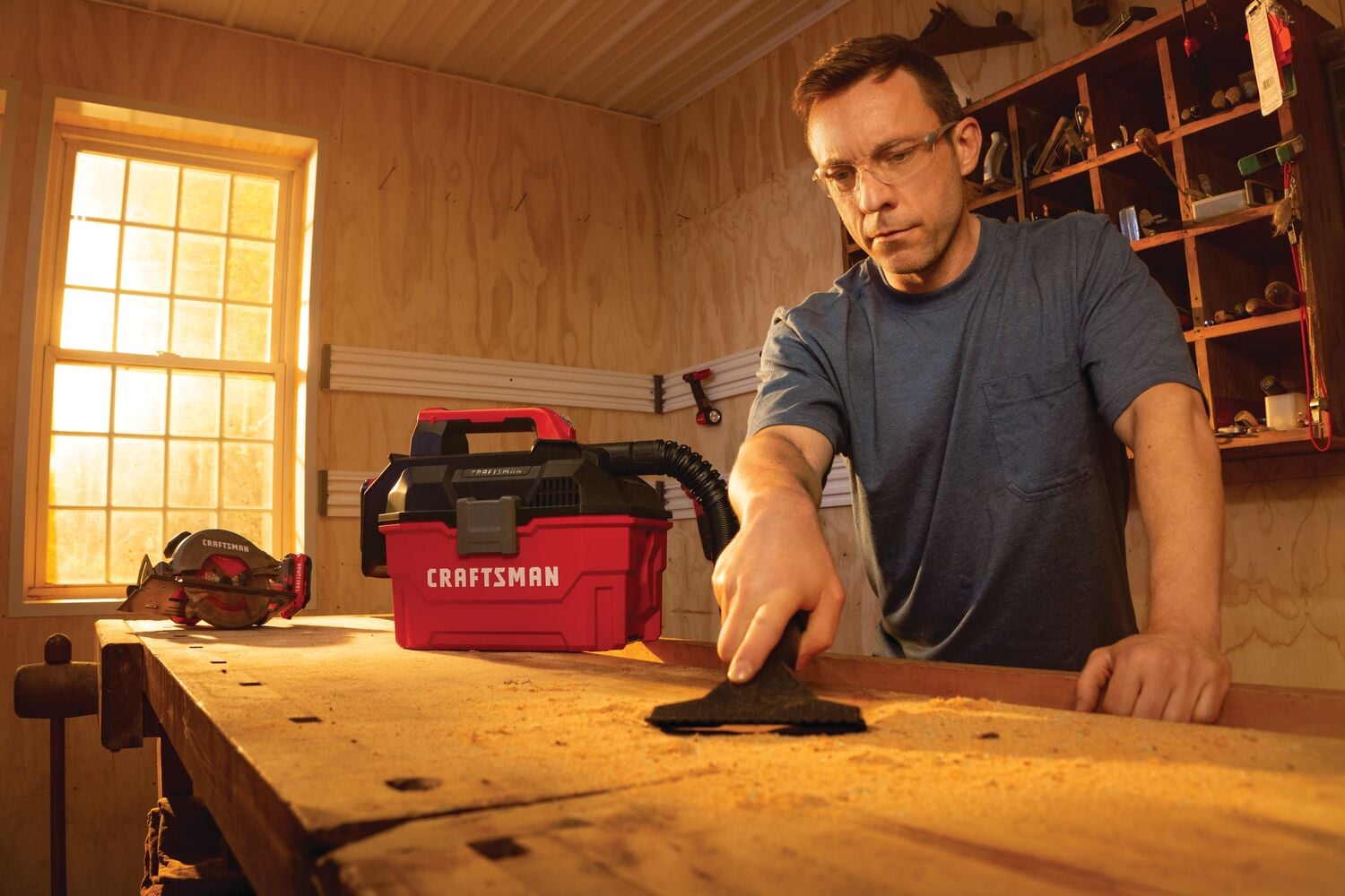 Photo of Craftsman wet/dry vacuum CMCV002B on workbench in a woodshop with a person cleaning sawdust.