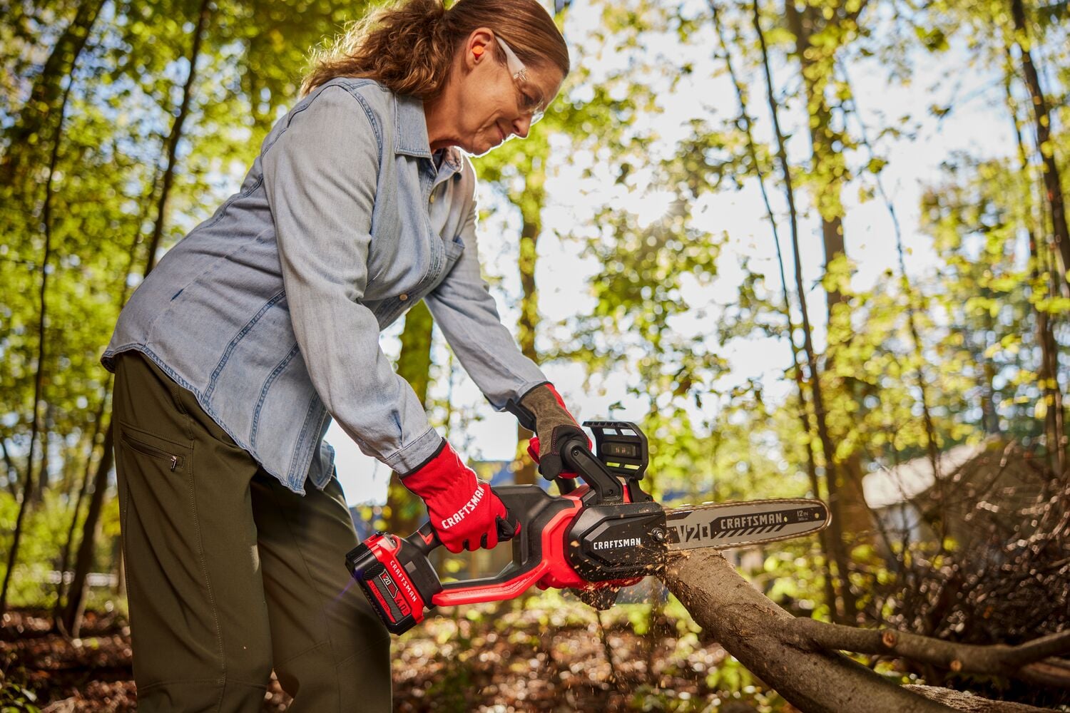 Photo of a person using a Craftsman cordless chainsaw, SKU CMCCS630B, cutting a tree branch outdoors.