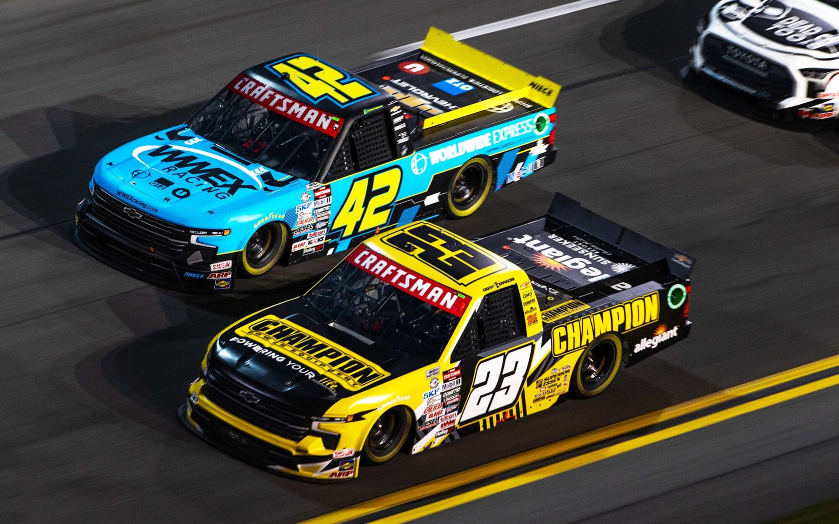 Photo of Craftsman branded race trucks, number 42 in blue and number 23 in yellow, side view on track.