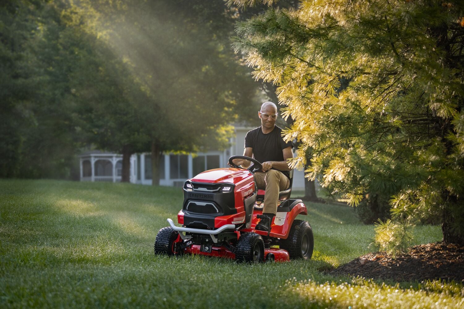 Photo of Craftsman riding lawn mower CMCRM233303 in red, operated on a grassy lawn near trees.