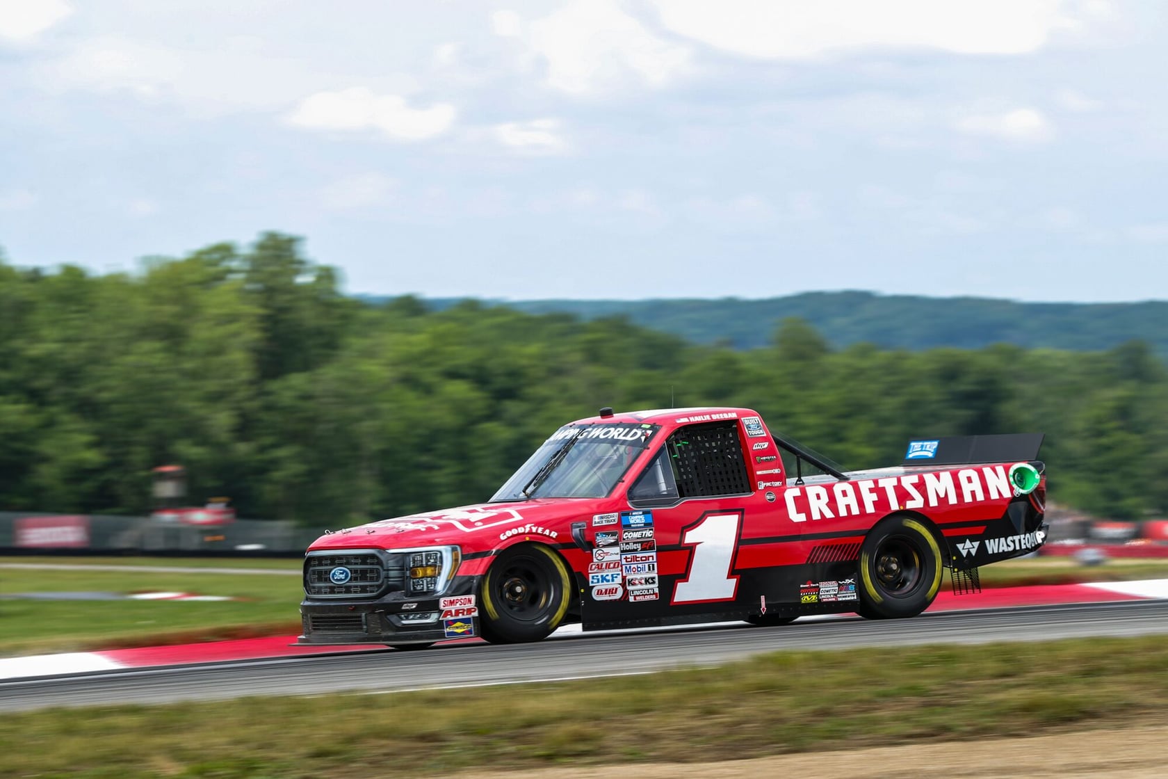 Photo of a red CRAFTSMAN-branded race truck, number 1, driving on a racetrack with greenery in the background.