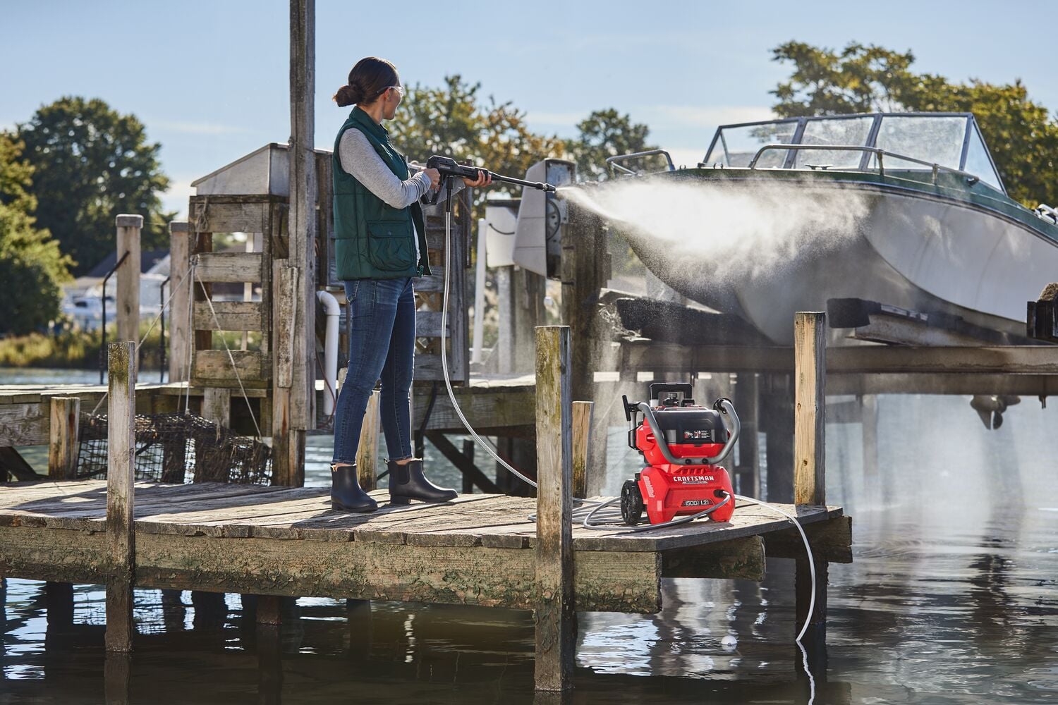 Photo of a person using a red CRAFTSMAN CMCPW1500N2 pressure washer to clean a boat on a dock by the water.