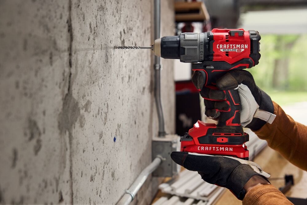Photo of Craftsman cordless drill CMCD726B drilling into concrete wall, held by gloved hand in workshop.