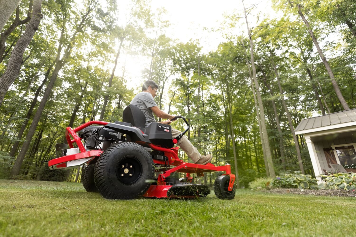 Photo of Craftsman zero-turn riding mower CMXGNAM211702 in use on a lawn, side angle, with trees in background.