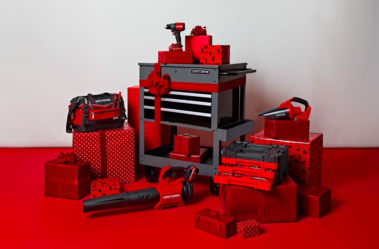 An assortment of CRAFTSMAN products like a utility cart, blower, mech set, vacuum, and tool bag placed around holiday decoration