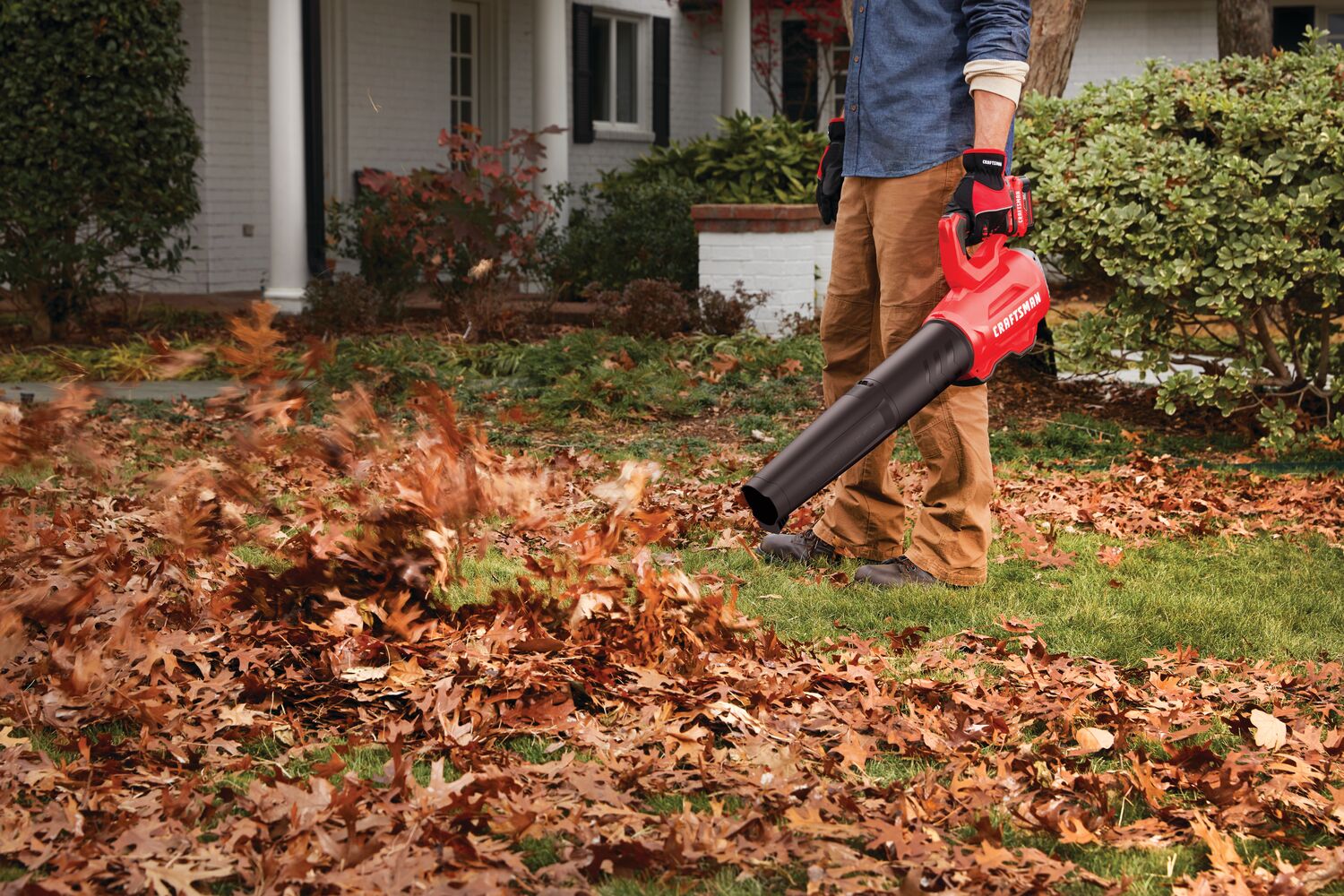 Brushless cordless axial blower kit 4 amp hour being used for cleaning dead leaves from lawn.