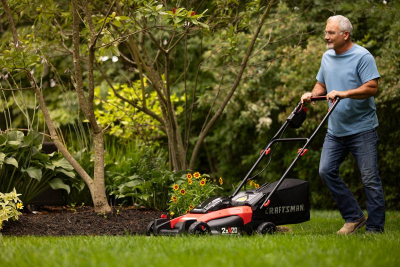 2 x 20 volt 20 inch brushless cordless push mower being used for mowing under bench.